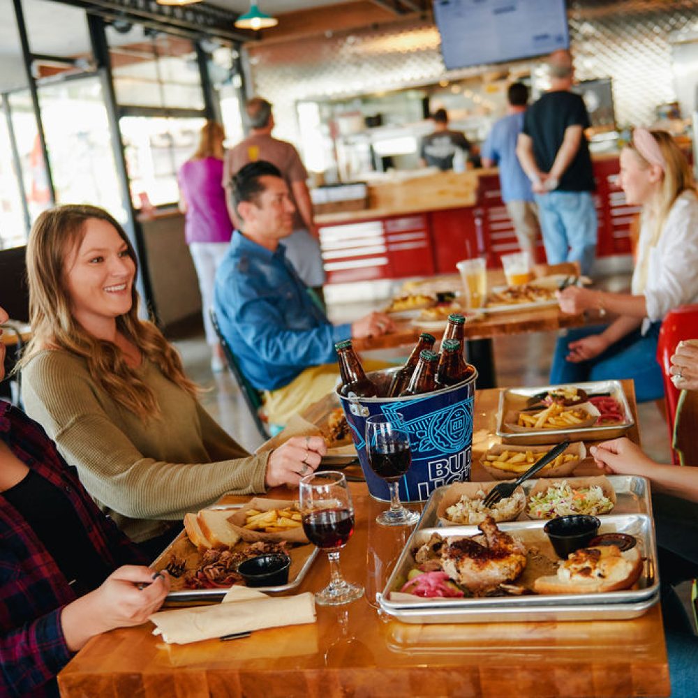 alt=" A group of friends enjoying some platters of BBQ with beers and wine on Smokey and the Brisket"